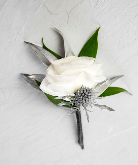 This boutonniere features an elegant ivory bloom paired with greenery and accents of silver, making the perfect finishing statement to any silver-inspired outfit! 