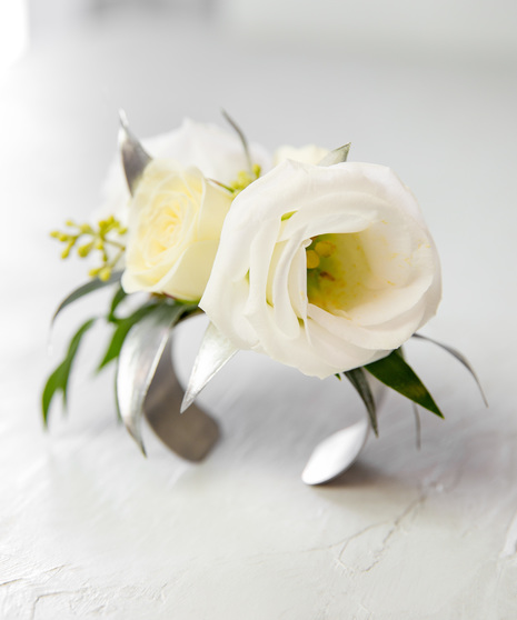 This corsage features elegant ivory blooms paired with greenery and accents of silver, all carefully designed on a metallic silver metal cuff.