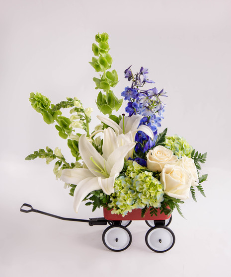 A blue and ivory arrangement designed in a mini keepsake red wagon. 