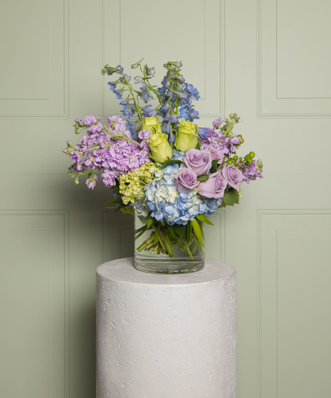 This beautiful arrangement includes lavender roses, spray stock, lime green roses, light blue delphinium, hydrangea, green hypericum, In a glass cube vase.