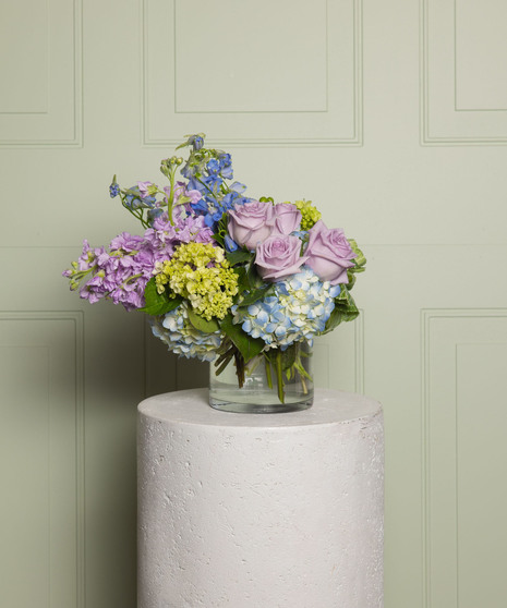 This beautiful arrangement includes lavender roses, spray stock, lime green roses, light blue delphinium, hydrangea, green hypericum, In a glass cube vase.