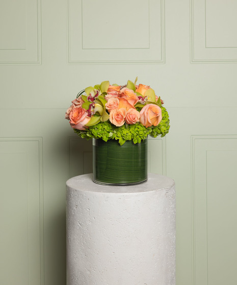 Cymbidium orchids, orange ranunculus, pink roses, green dianthus and succulents, brought together in a leaf lined, modern pave style vase.